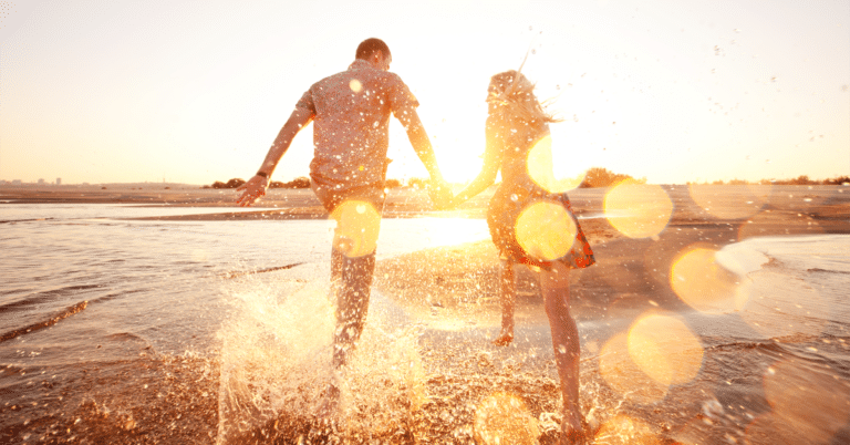 A couple practicing relationship tricks while running in the water at sunset.