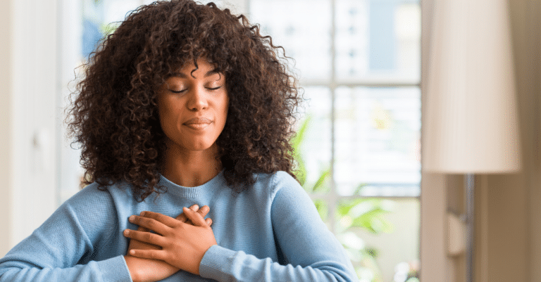 A woman with curly hair expressing gratitude by holding her chest with her hands.