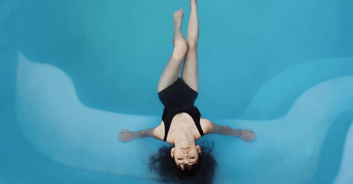 A woman enjoying relaxation in a black swimsuit, floating in a serene blue pool.