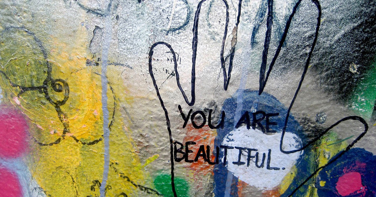 A graffiti-covered wall promoting self-esteem with the message "you are beautiful.