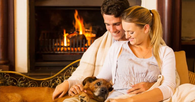 A couple sharing love and warmth alongside their dog by a fireplace.