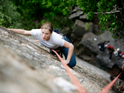 A woman believes in herself as she climbs up a rock with a rope.