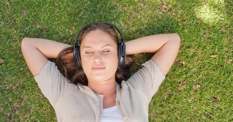 A woman laying on the grass listening to music, peacefully and blissfully embracing the therapeutic melodies.
