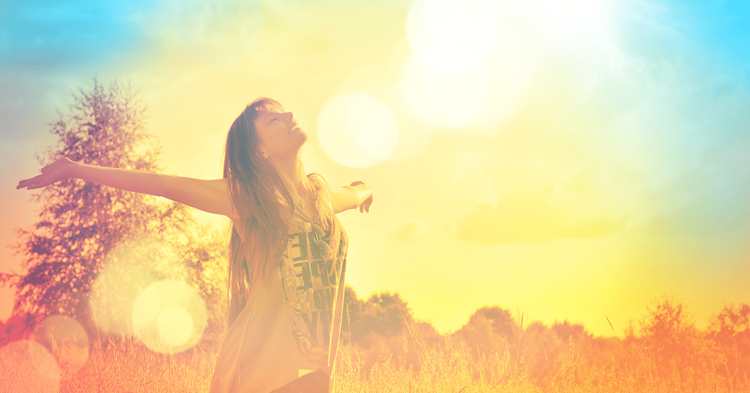 A woman is standing in a field, embodying positive energy with her arms outstretched.
