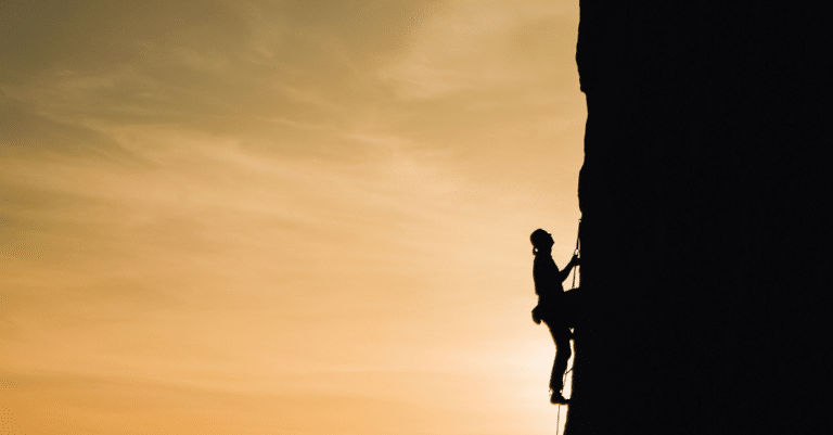 A silhouette of a climber scaling a cliff at sunset, demonstrating the essence of self-determination.