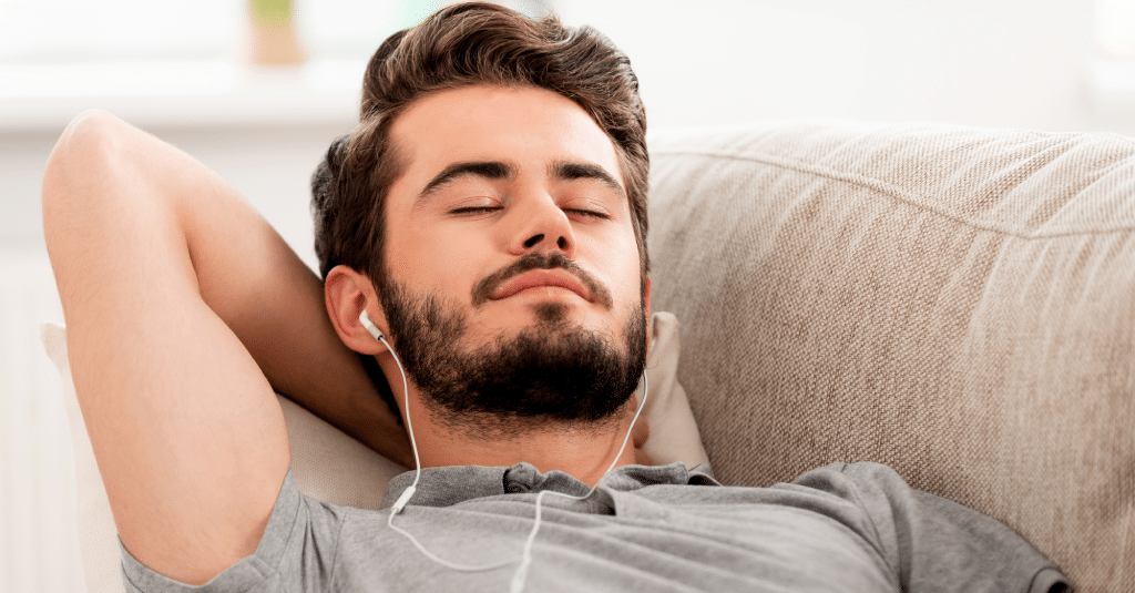A man comfortably dozing on a couch while listening to binaural beats with headphones.