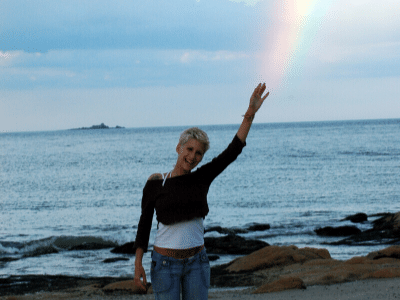 A woman standing on a beach with a rainbow in the sky, inspiring others to believe in themselves.
