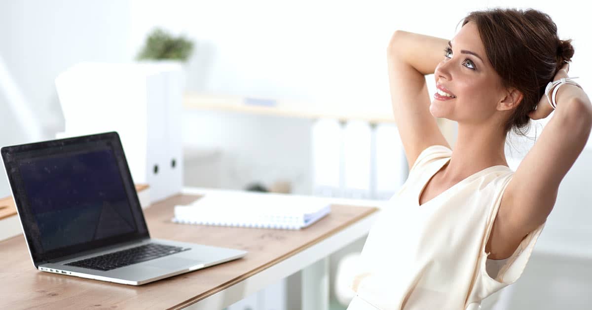 A woman practices the law of attraction in her workplace while relaxing in front of her laptop.