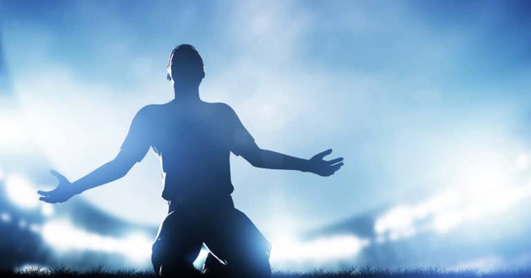 A victorious silhouette of a soccer player with his arms outstretched.