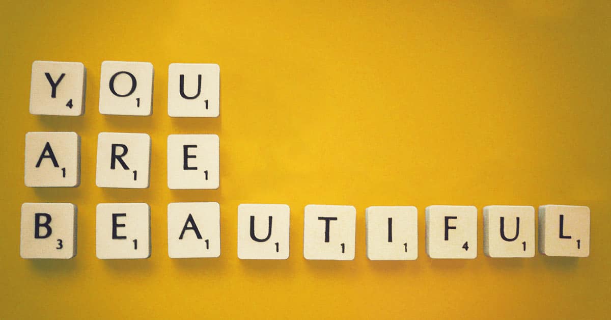 You are beautiful written in scrabble tiles on a yellow wall.