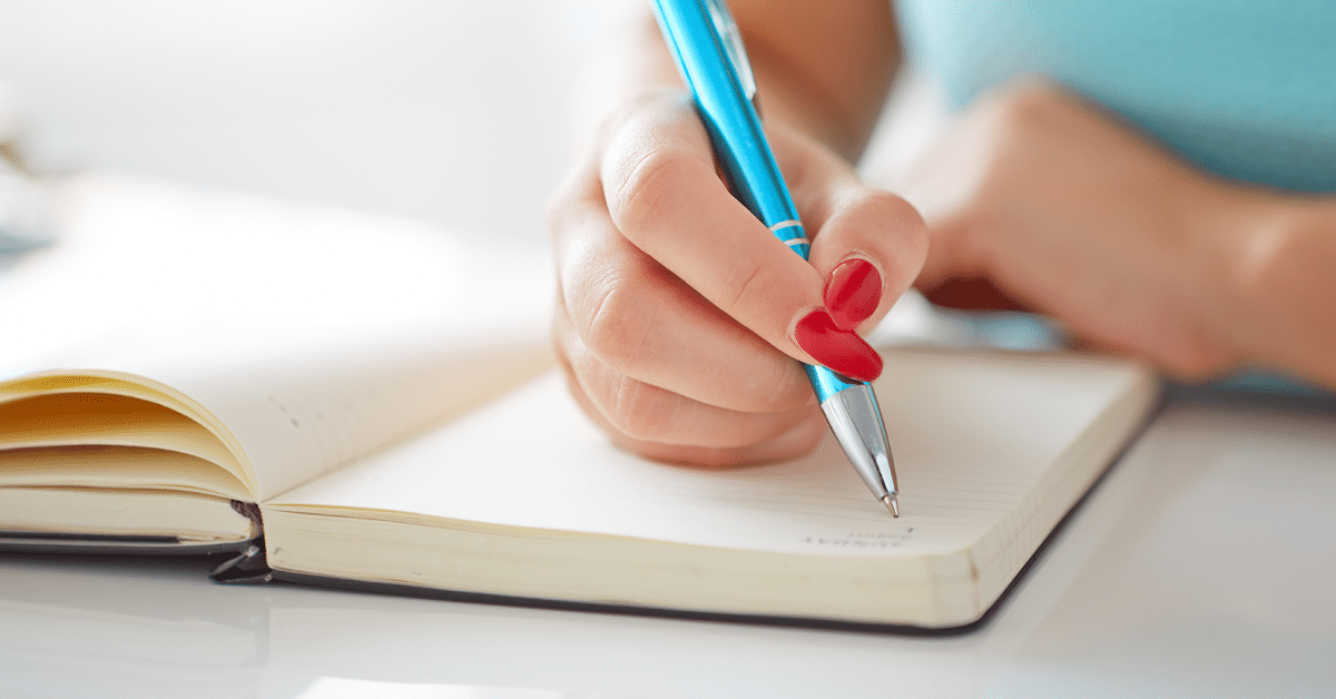 A woman, pen in hand, writes in a notebook - a letter to her younger self.