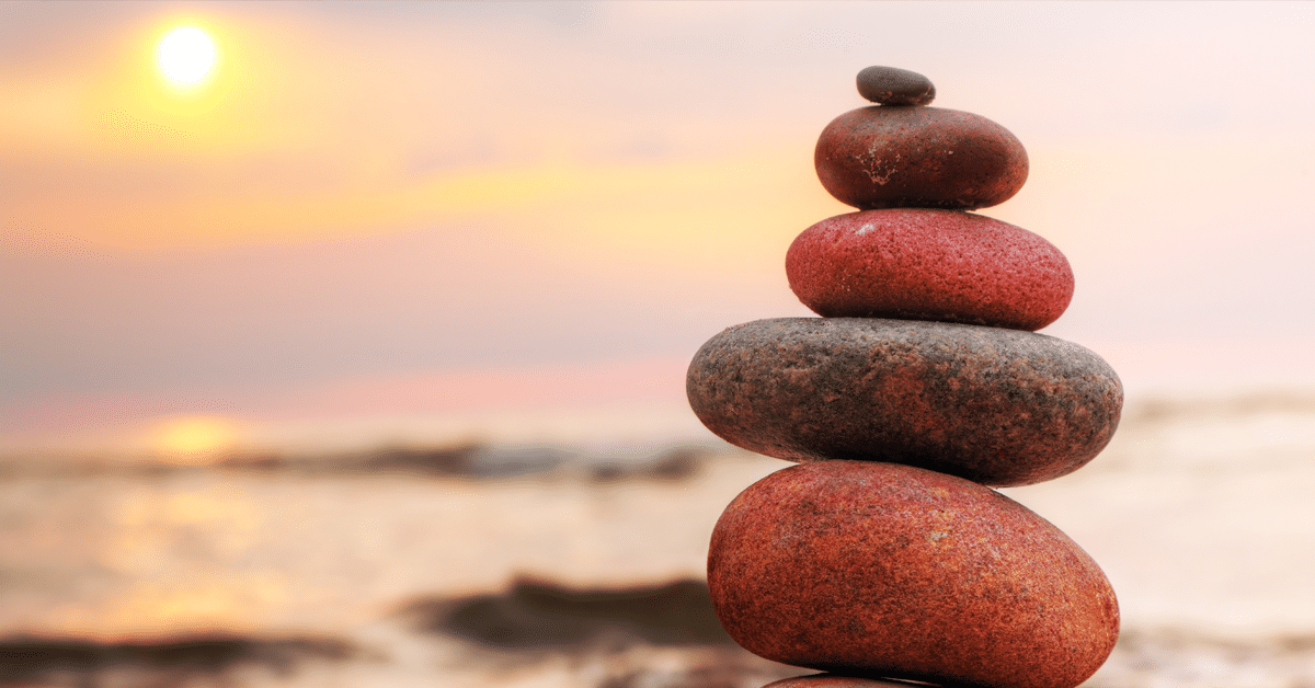 A re-centered stack of rocks on the beach at sunset.