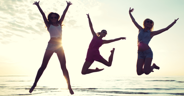 Three young women experiencing happiness as they jump on the beach at sunset.