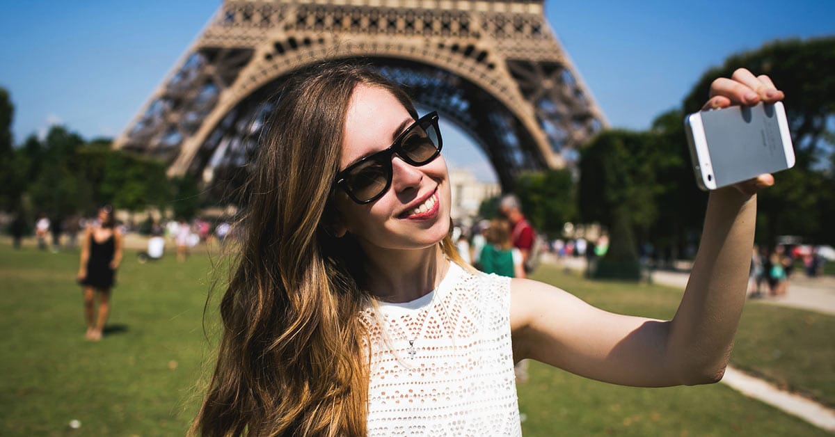 A woman is capturing a selfie to manifest the connection in her long-distance relationship amid the grandeur of the Eiffel Tower.