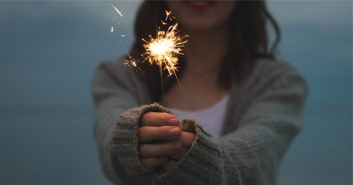 A woman boosting her vibration as she holds a sparkler in her hand.