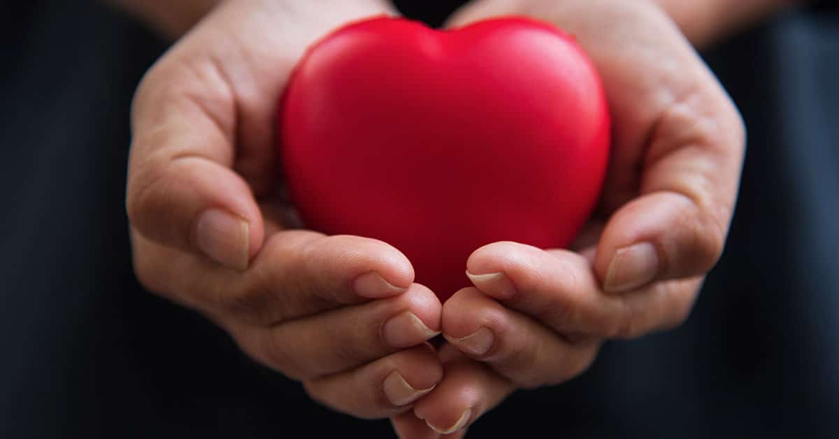 A person displaying wisdom and compassion while holding a red heart in their hands.