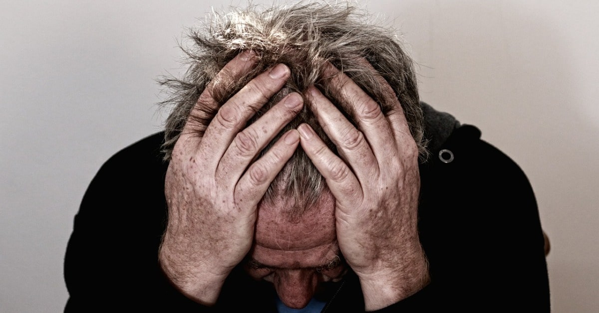 A man overwhelmed by negative chatter, with his hands on his head.