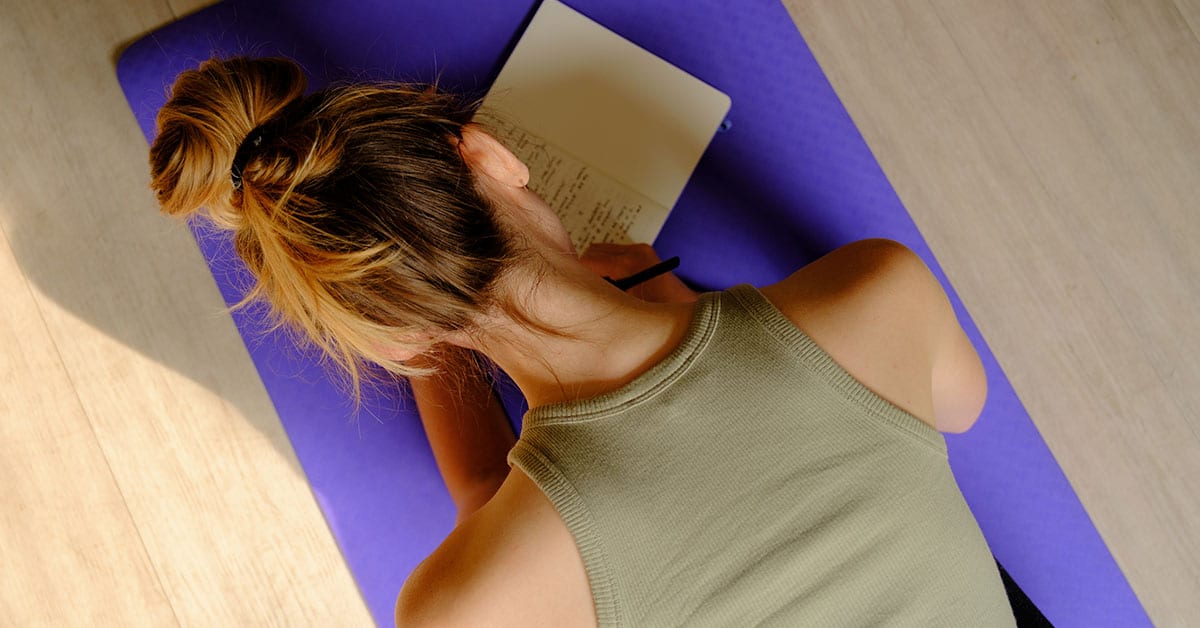 A woman writing her inner journey on a yoga mat to preserve her dream journal.