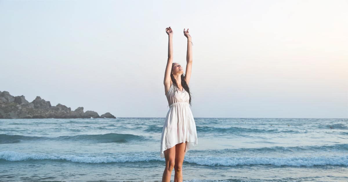 A successful woman standing on the beach, her arms raised in triumph.