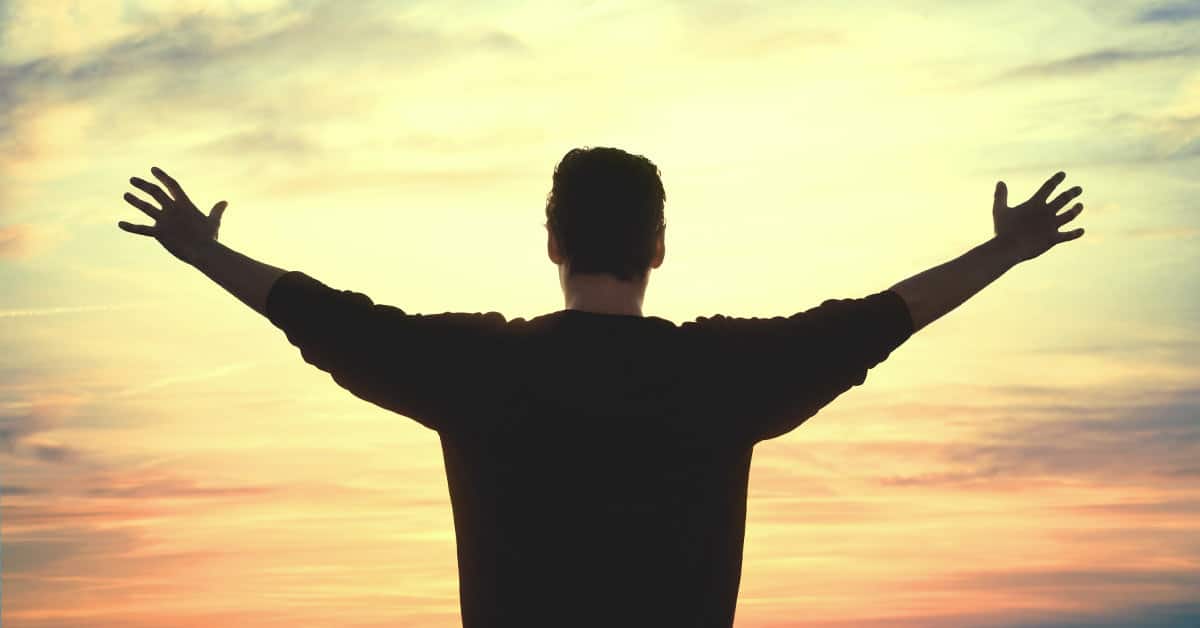 A man reclaiming his power stands with arms outstretched towards a mesmerizing sunset.