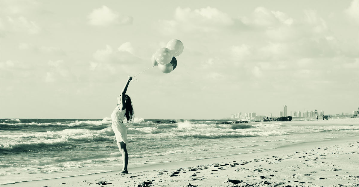 A woman on the beach learns how to let go by releasing a white balloon.