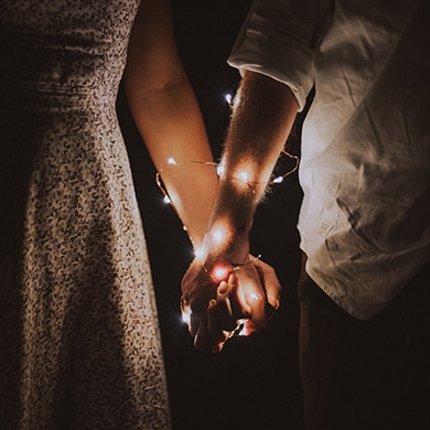 Man and woman holding hands with fairy lights around their arms