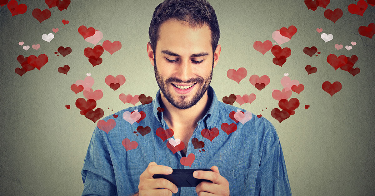 A man engrossed in online dating, looking at a cell phone with hearts flying around him.