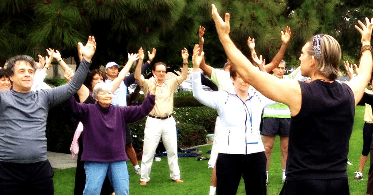 A group of people practicing qigong, raising their hands in the air.