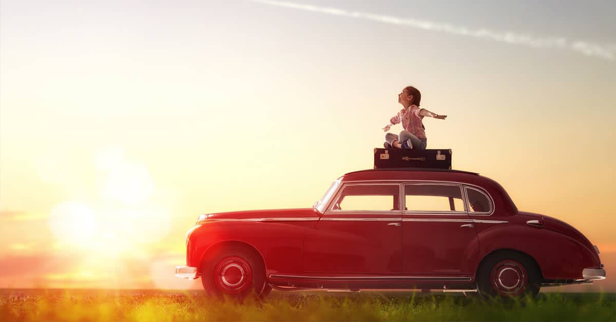 A girl with an open mind is sitting on top of a red car at sunset.