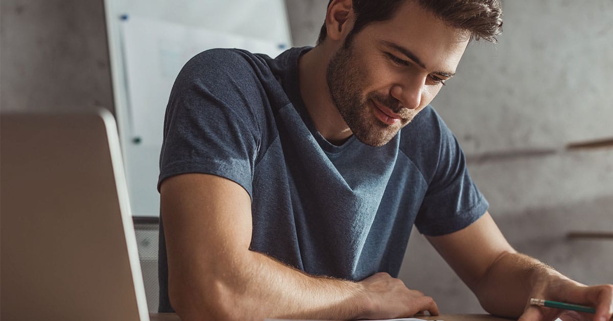 A man using art to enhance self-knowledge while sitting at a desk with a laptop and a pen.