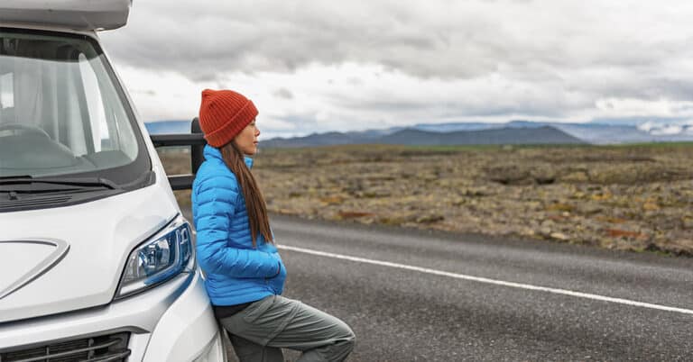 A woman is increasing her self-reliance as she leans against the side of a white RV.