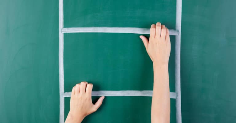 A woman's hand signaling readiness by reaching up a ladder on a blackboard.
