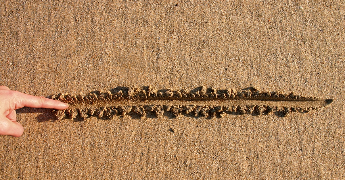 A person is using gestures to specify the limits of a designated area in the sand.