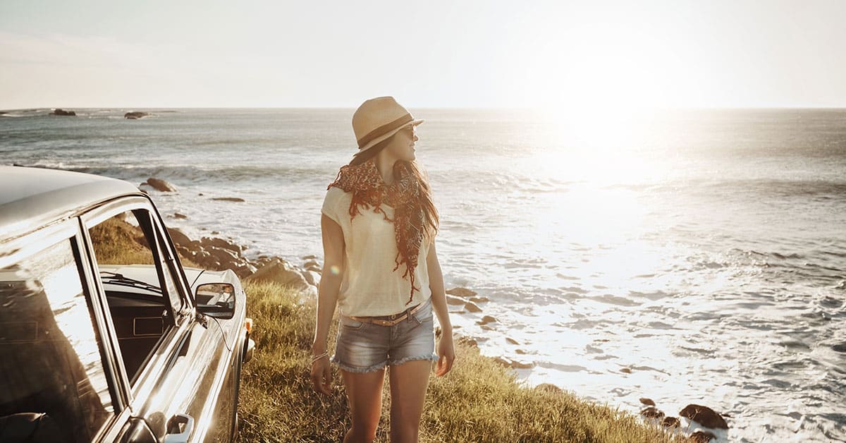 A woman is standing next to a car near the ocean, experiencing positive results.