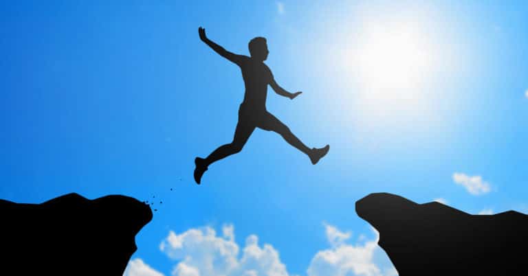 A silhouette of a man turning failure into success by jumping over a cliff.