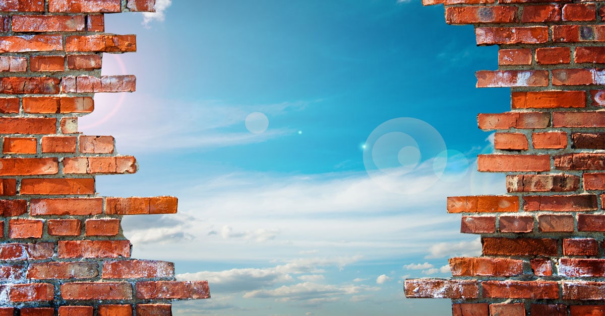 A sky peeking through a hole in a brick wall symbolizes overcoming obstacles in achieving goals.